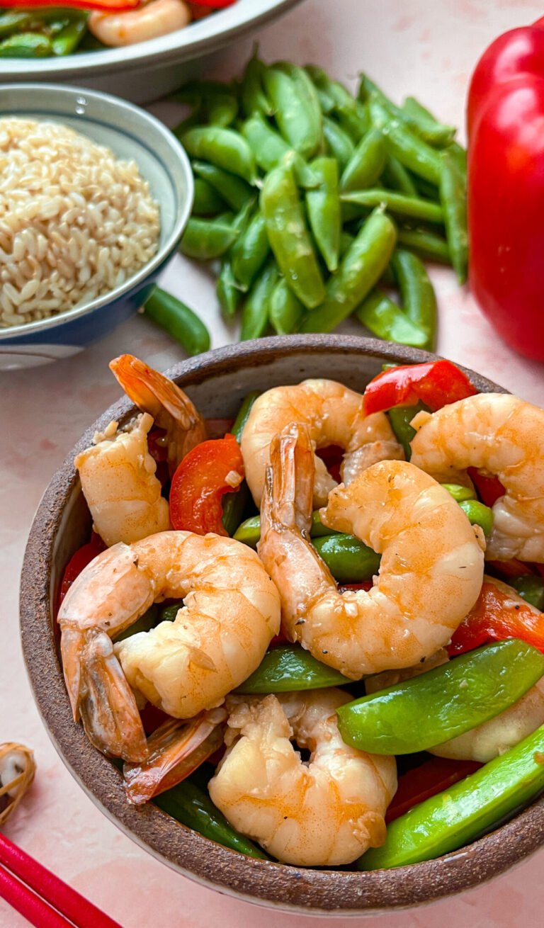 stir-fry shrimp with snap peas surrounded by a bowl of brown rice, and a large serving bowl of the dish