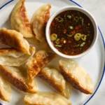 soy and vinegar dumpling suace in a small ramekin on a plate with fried dumplings on a kitchenb countertop