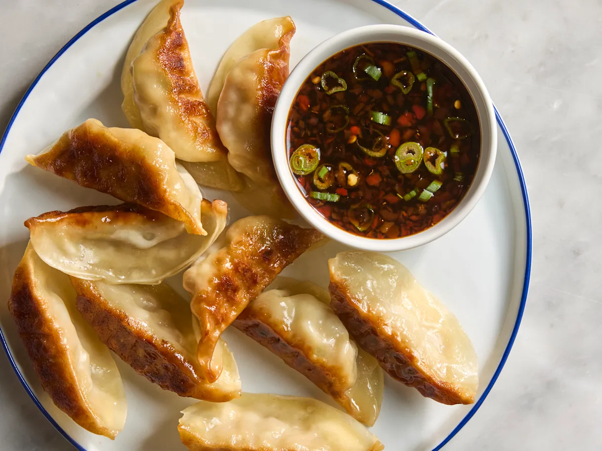 soy and vinegar dumpling suace in a small ramekin on a plate with fried dumplings on a kitchenb countertop